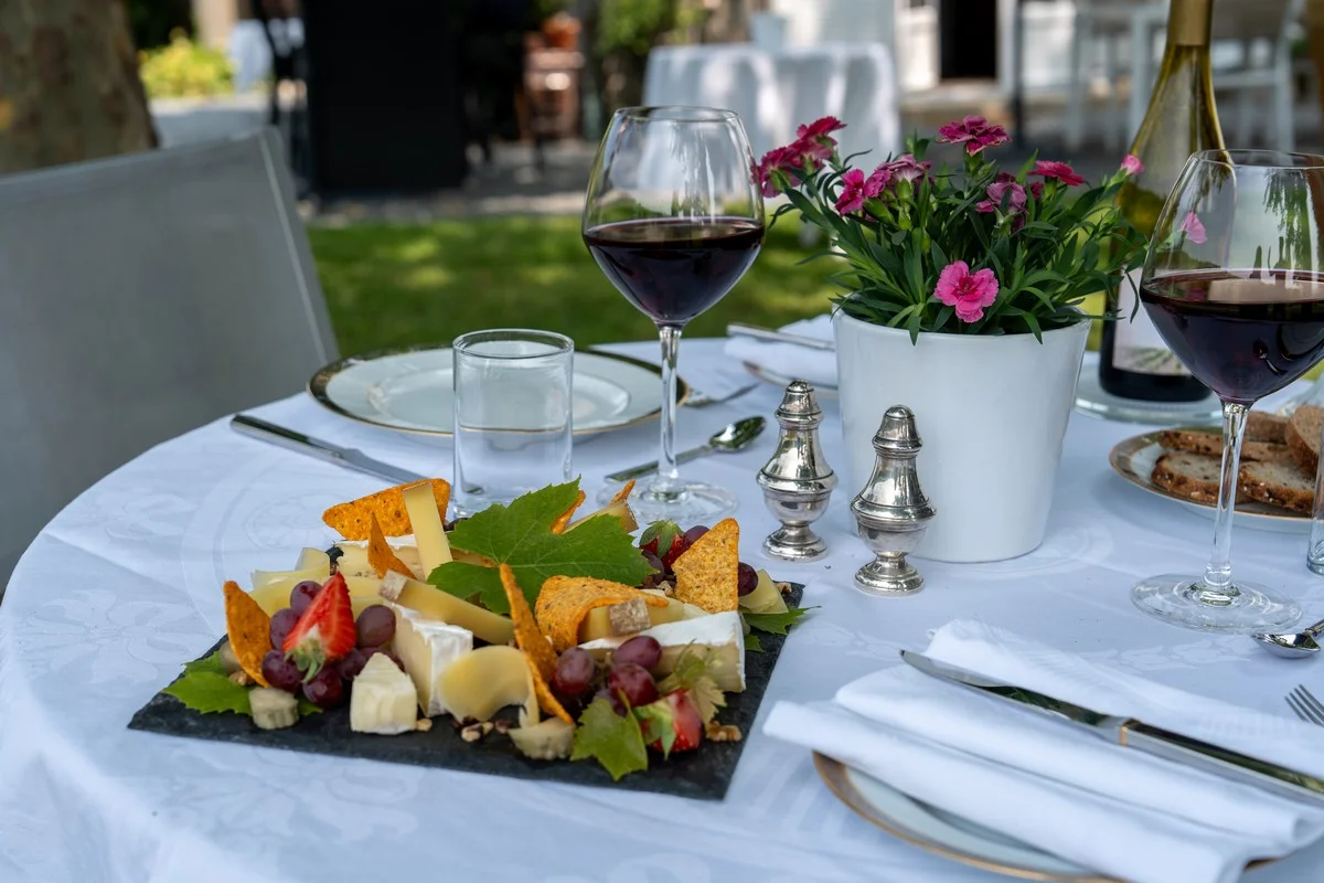 Im Garten für das Abendessen gedeckter Tisch: Beaujolais-Weingläser, Käseplatte und sorgfältig angerichtetes Gedeck